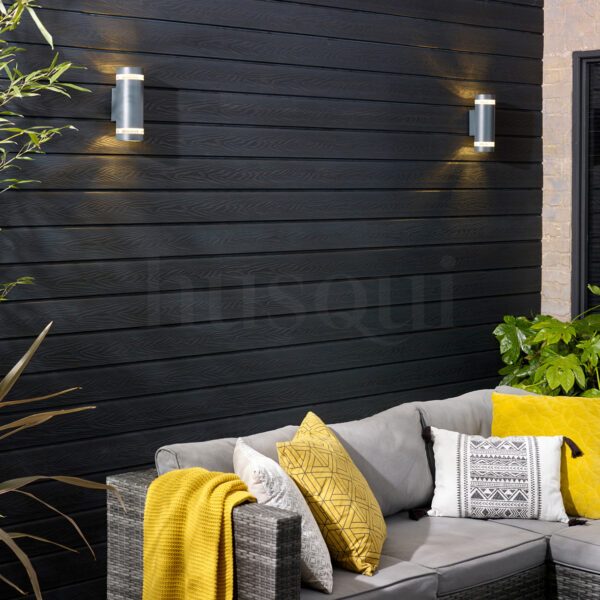 Black cladding exterior wall with two gunmetal up/down lights behind a sofa with grey and yellow cushions