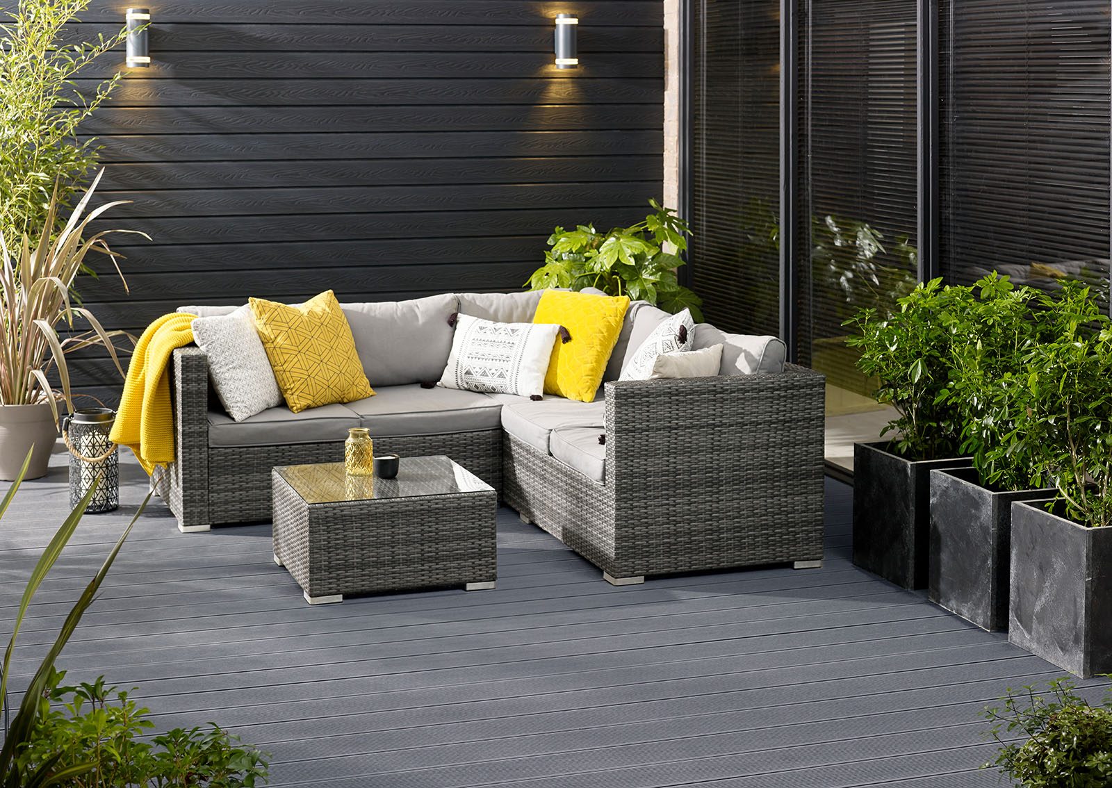 Husqui grey decking in courtyard with wicker corner sofa, plants and black clad exterior wall