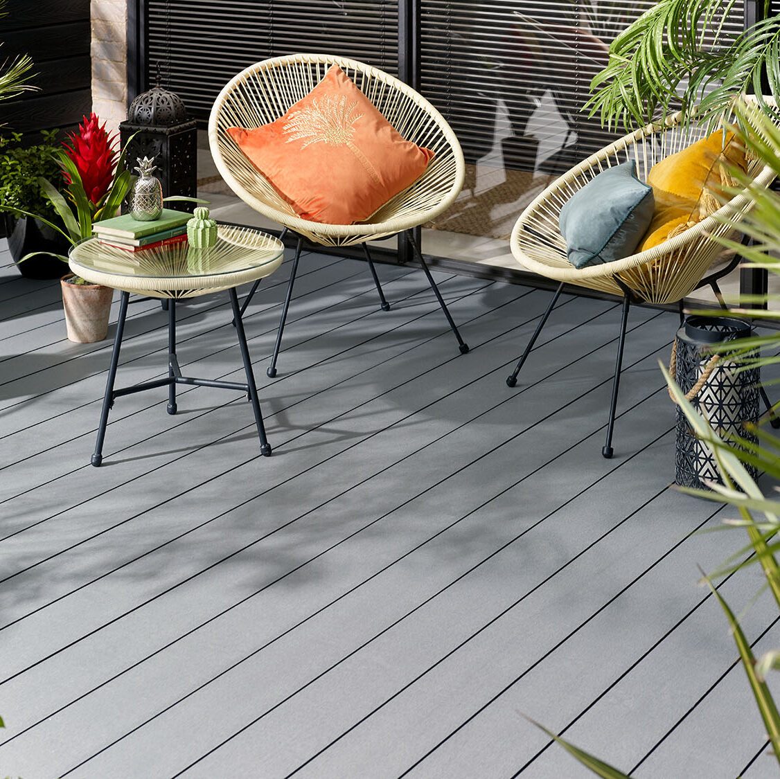 Grey wood grain decked courtyard with two cream chairs and table surrounded by plants