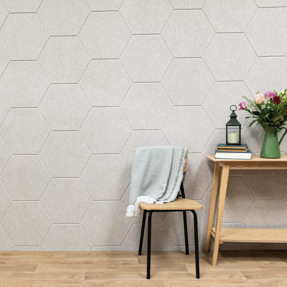 A wall covered in Husqui hexagonal acoustic wall panels in taupe with a light oak chair and side table in front.